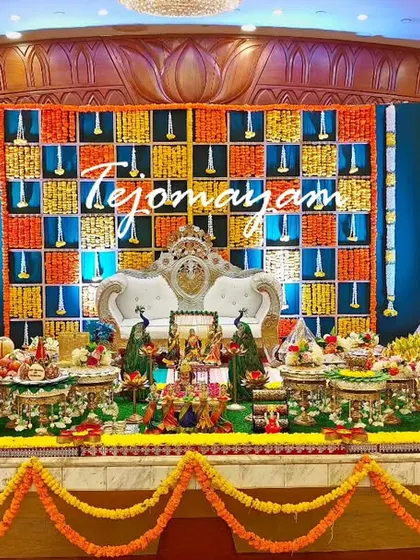 A beautiful baby shower stage with a colorful floral checkerboard backdrop, peacock figures, and a full display of traditional plates.