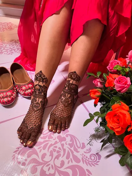 The bride's feet are adorned with intricate henna, featuring jharokha and elephant motifs that match her hand designs, seen in other photos. This shot is paired with her beautiful juttis.