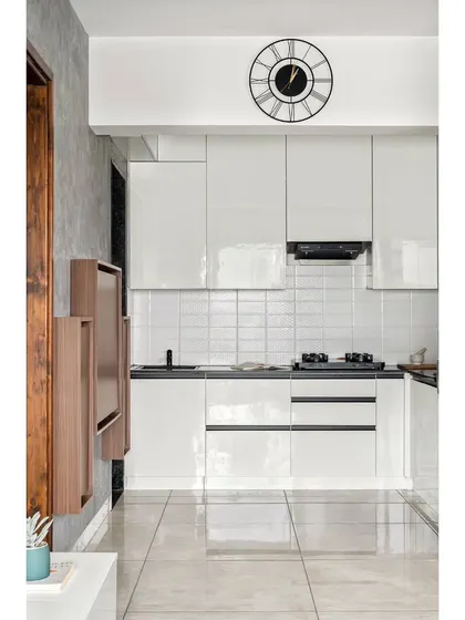 The all-white kitchen in the 'Nordic Grey Apartment' uses high-gloss laminate to reflect light and create a sense of spaciousness. The jet-black granite countertop provides a sharp, modern contrast.