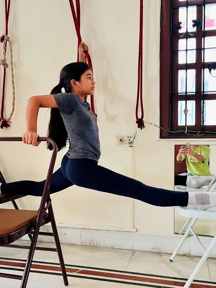 A side view of a student holding a supported split between two chairs. This exercise is excellent for building hip flexibility and strength for dance and gymnastics.