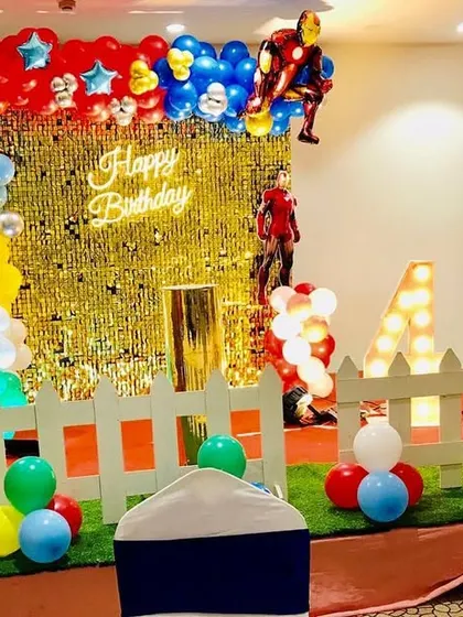 An Avengers-themed birthday party with a gold shimmer wall. The decor includes Iron Man and Captain America props and a colorful balloon arch.