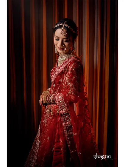 A full-length shot of the bride in her stunning red lehenga, with the warm, striped background adding to the richness of the image.