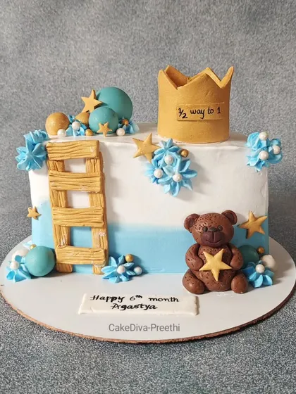 This cake celebrates a baby's half-birthday, "1/2 way to 1". The design includes a fondant teddy bear, a ladder, stars, and a crown, marking this sweet milestone.
