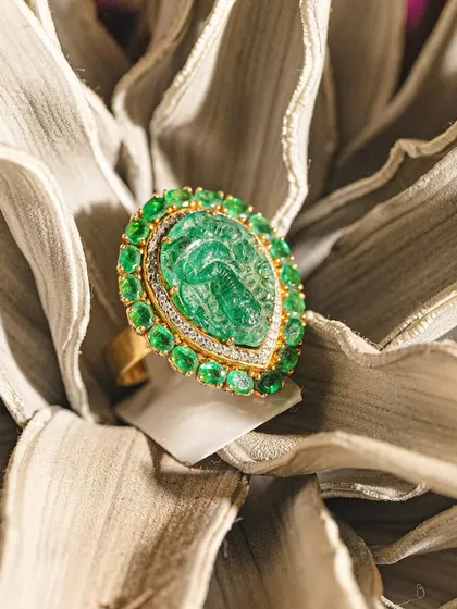 A true work of art. This statement ring features a hand-carved emerald depicting a deity, surrounded by a halo of smaller emeralds.