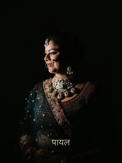 A dramatic, low-key portrait of the bride Payal, with her name in Hindi text. The lighting highlights her jewelry and profile beautifully.