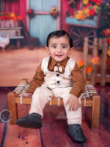 This little boy looks charming in his vest and bow tie, seated on a miniature charpai for a rustic, barnyard-themed shoot.