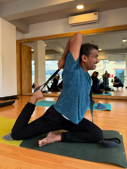 A student smiles as he uses a strap in Eka Pada Rajakapotasana (One-Legged King Pigeon Pose) to open his chest and shoulders.