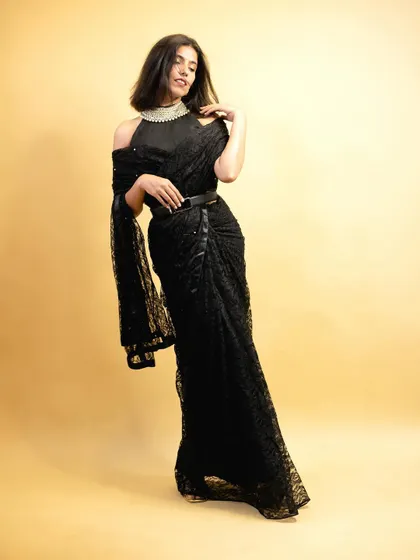 A full-length studio shot of a modern black lace saree, styled with a belt to create a chic, defined silhouette for party wear collections.