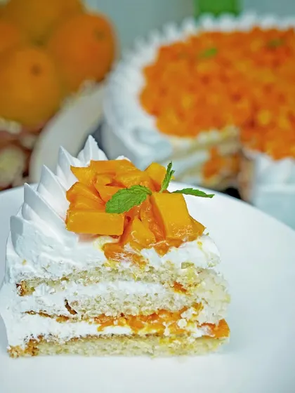 A perfect slice of fresh mango cake on a white plate, showing the layers of cream and fruit. This classic food shot highlights the freshness and texture of the dessert.