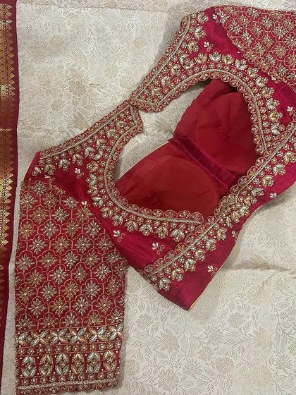 A flat-lay of a red bridal blouse, showing the embroidery-covered sleeve and the detailed work around the neckline.
