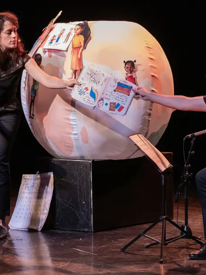 A performance of 'Pajarillo Verde' on a formal stage, showing the use of props and illustrated books. The show is adaptable to both indoor and outdoor venues.