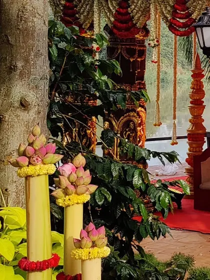 A beautiful outdoor wedding setup by the water. The traditional mandap pillars and lotus floral arrangements are complemented by the natural scenery and classic lamp posts.