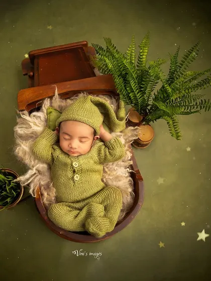 An earthy and natural theme, with the baby dressed in a cute green pixie-style outfit. The use of wooden props and ferns creates a serene, woodland atmosphere.