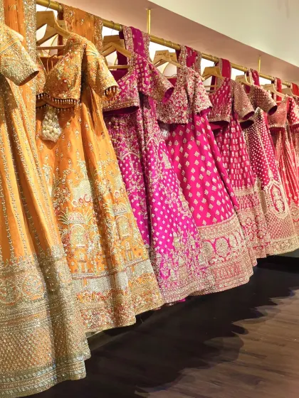 A rack of our curated lehengas, showcasing the spectrum of colours and craftsmanship available. From deep jewel tones to warm oranges and bright pinks, each piece is waiting for its moment.