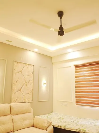 A cozy family room or den with a recliner sofa and simple wall decor. The false ceiling with recessed lighting provides a comfortable and relaxed atmosphere.