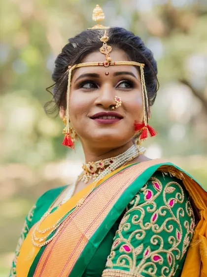 A portrait of a graceful Maharashtrian bride. Her look features a neatly tied bun, traditional gold jewelry, and makeup that highlights her natural elegance against a beautiful outdoor backdrop.