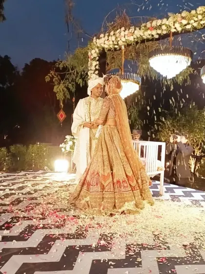A magical Varmala moment under a floral arch with hanging chandeliers, as petals shower the happy couple.