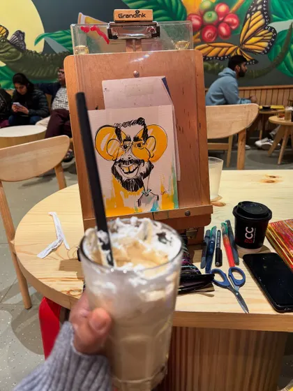 My setup at The Black Coffee Cafe, with a finished caricature on the easel and a refreshing drink to keep me going.