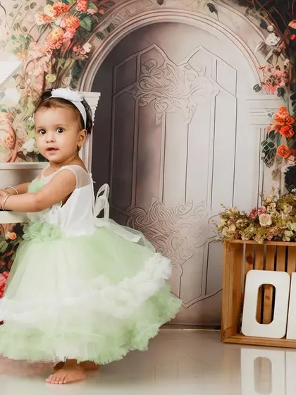 Dressed in a lovely pastel green dress, this little girl is ready to play a tune to celebrate her first birthday. The floral backdrop adds a touch of garden magic.