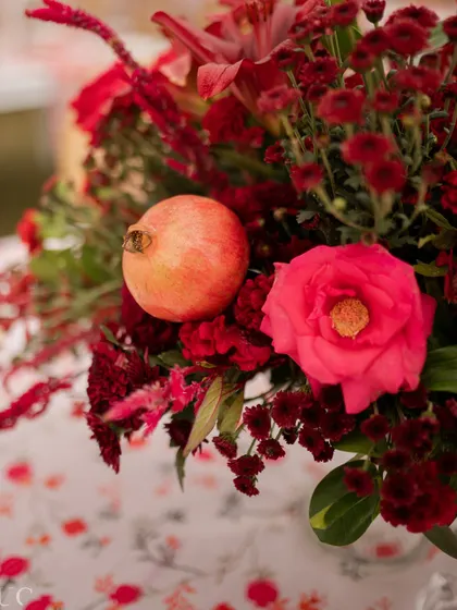 A close-up of a floral arrangement from the 'Gulnar' Mehendi, featuring a real pomegranate nestled among red flowers.