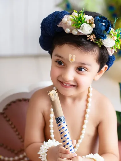 A sweet, close-up portrait of a smiling little Krishna holding his flute. His bright eyes and happy expression are the focus of this beautiful shot.