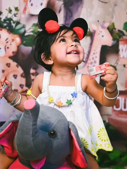 Ready for a jungle adventure, this little one sits on a plush elephant, creating a cute and imaginative scene.