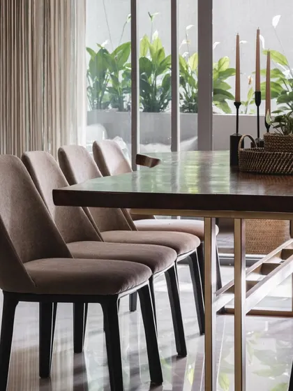 The formal dining area features plush, comfortable chairs and a live-edge wooden table, set against a view of the green planters on the deck.