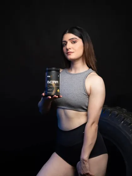 A female model holding a BCAA supplement, with a confident and strong posture against a dark, moody background.
