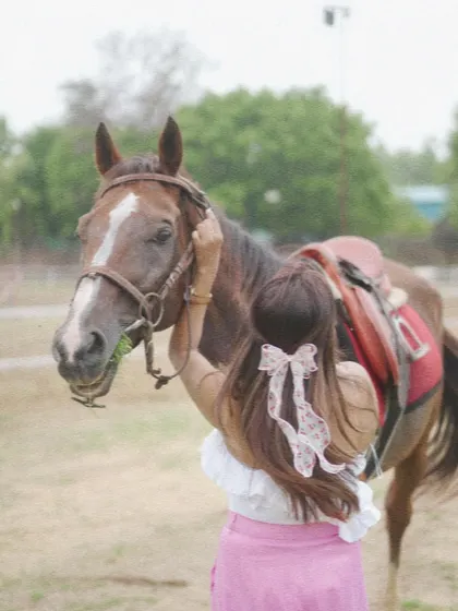 A rider adjusts her horse's bridle while it enjoys a snack. This shows the everyday care and connection at our stables.