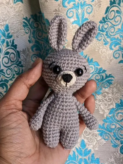 The little grey bunny keychain against a patterned background.