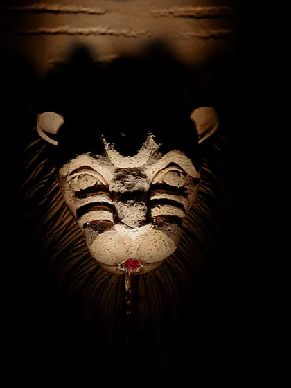 A close-up of a lion head wall mount, a symbol of strength and nobility used in ancient Roman gardens. The dramatic lighting creates a sense of mystery and power.