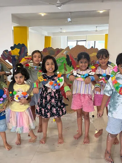 A group of young artists showing off the colorful, textured necklaces they designed. This activity focuses on fine motor skills and personal expression through wearable art.