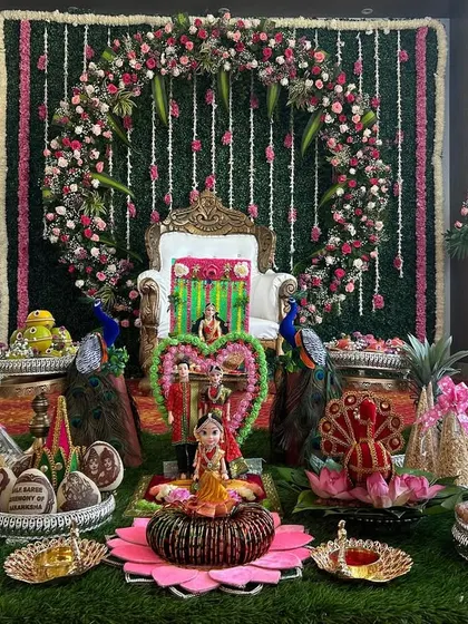 An exceptionally detailed Seemantham setup. It features a circular floral arch on a greenery wall, peacock statues, and an elaborate display of decorated plates and lotus-themed items.