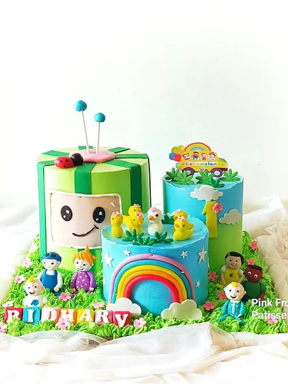A vibrant, deconstructed Cocomelon cake for a first birthday. This multi-cake display features the iconic Cocomelon TV, a rainbow, and all the main characters as handmade figurines.