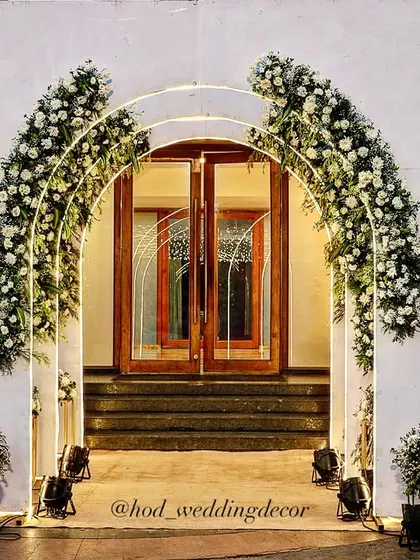 A modern and elegant entrance archway adorned with white flowers and subtle lighting. The clean lines of the arch combined with the softness of the florals create a balanced and sophisticated look.