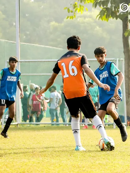 A player in an orange jersey looks to dribble past a defender.