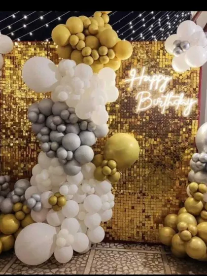 A stylish birthday backdrop with a gold sequin wall and white neon sign. The balloon decor features a modern color palette of white, grey, and gold, arranged asymmetrically for a contemporary feel.