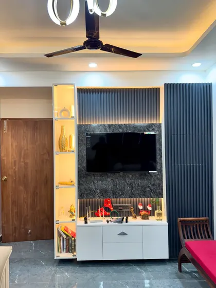 A complete TV unit design in a finished home. It features a dark marble-look panel, fluted accents, and a lit glass display cabinet for books and decor items.