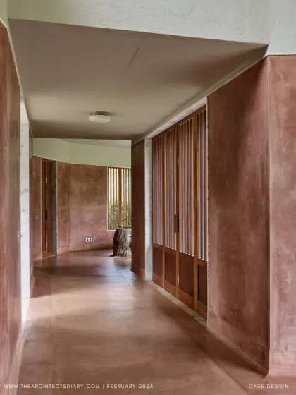 The corridor at Villa Uma is a study in texture and light. The curved, pigmented plaster walls guide you through the space, while slatted wooden screens filter the sunlight and offer glimpses of the garden beyond.