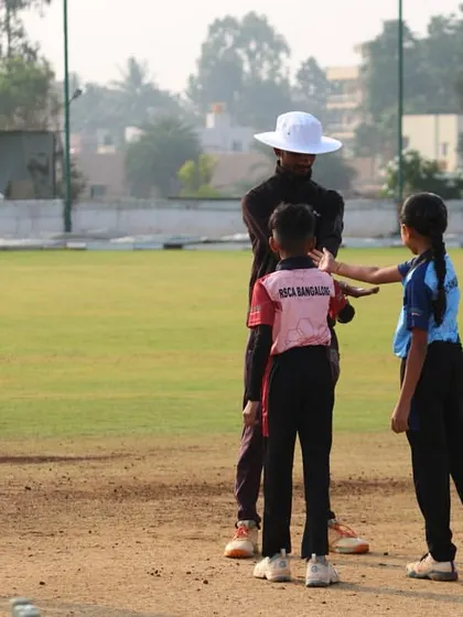 An umpire mediates the toss between two young players, a boy and a girl, showcasing our inclusive approach to youth cricket.