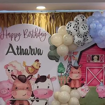 The top of a farm-themed birthday backdrop for Atharva. The design features cute cartoon farm animals and a balloon garland with cow-print accents.