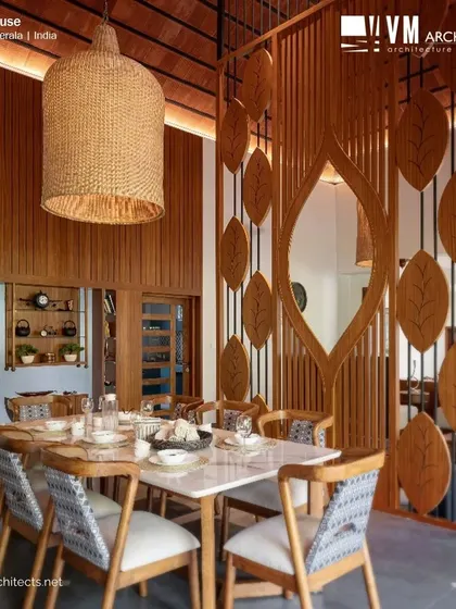 A detailed shot of the dining area in Kuttiyil House, highlighting the blend of textures from the wooden partition, marble tabletop, and patterned chair fabric.