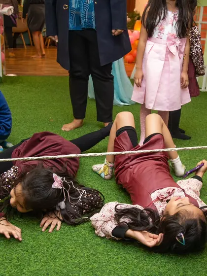 That's how it's done! Two girls expertly slide under the limbo rope, showing impressive flexibility and determination.