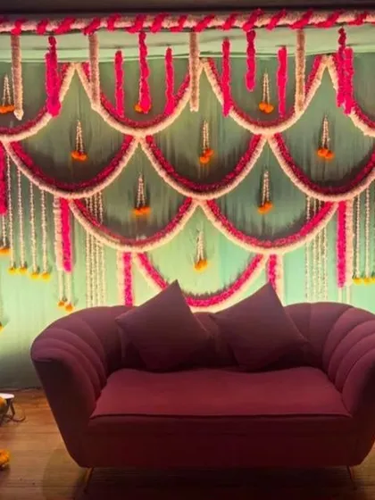 An elaborate backdrop made of flower garlands in scalloped patterns. The combination of pink and white flowers against a green background creates a rich and festive look.