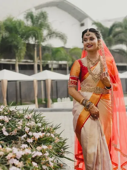 The vibrant red veil adds a beautiful pop of color to Brunda's classic off-white and gold saree.
