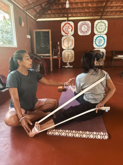 Using a yoga strap is a wonderful way to make challenging poses more accessible. Here, Neelam guides a student in a seated forward bend, demonstrating how props can help maintain alignment and deepen a stretch safely. We teach you to be a resourceful and inclusive instructor.