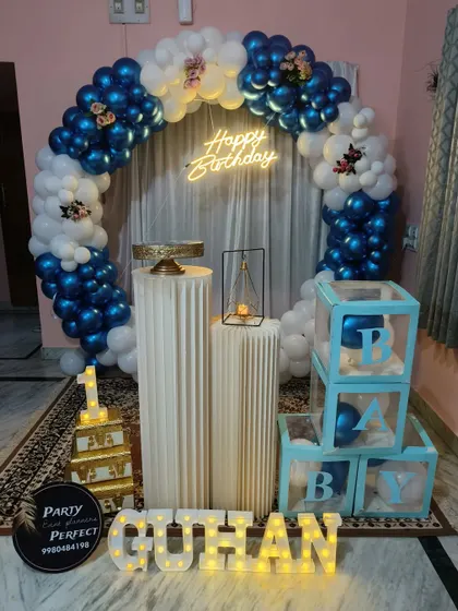 A classic blue and white balloon ring decoration for a boy's birthday, complete with a neon sign, 'B-A-B-Y' blocks, and personalized light-up name.