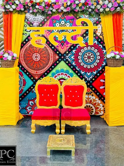 A vibrant and folksy Haldi backdrop. I used a colorful printed fabric panel with the 'Haldi' sign in Hindi, flanked by bright yellow drapes and traditional red and gold chairs.