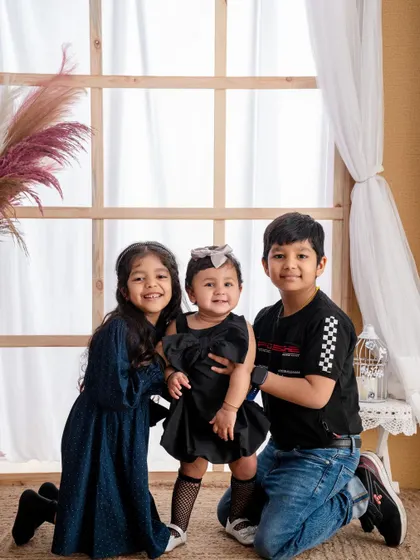 A lovely portrait of three siblings together. The older brother and sister protectively hold their baby sister, showcasing the beautiful dynamic in a larger family.