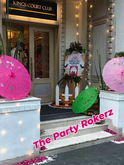 The entrance to a Teej celebration at Kings Court Club, decorated with colorful umbrellas, fairy lights, and a custom welcome board.